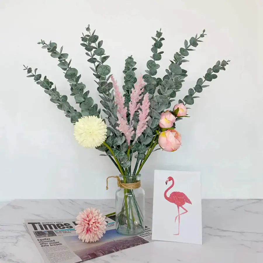 A clear glass vase with artificial eucalyptus greenery stems featuring pink and white blooms for living room decor