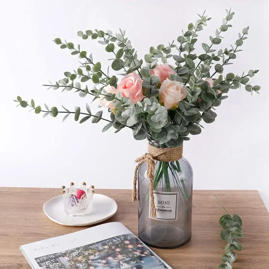 A translucent gray glass vase with rustic twine holds pink roses and decorbites artificial eucalyptus leaves