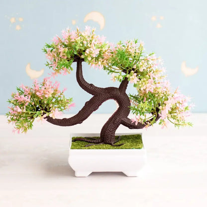 Artificial bonsai tree with dark brown trunk, pink blossoms, green foliage in white ceramic pot with artificial grass