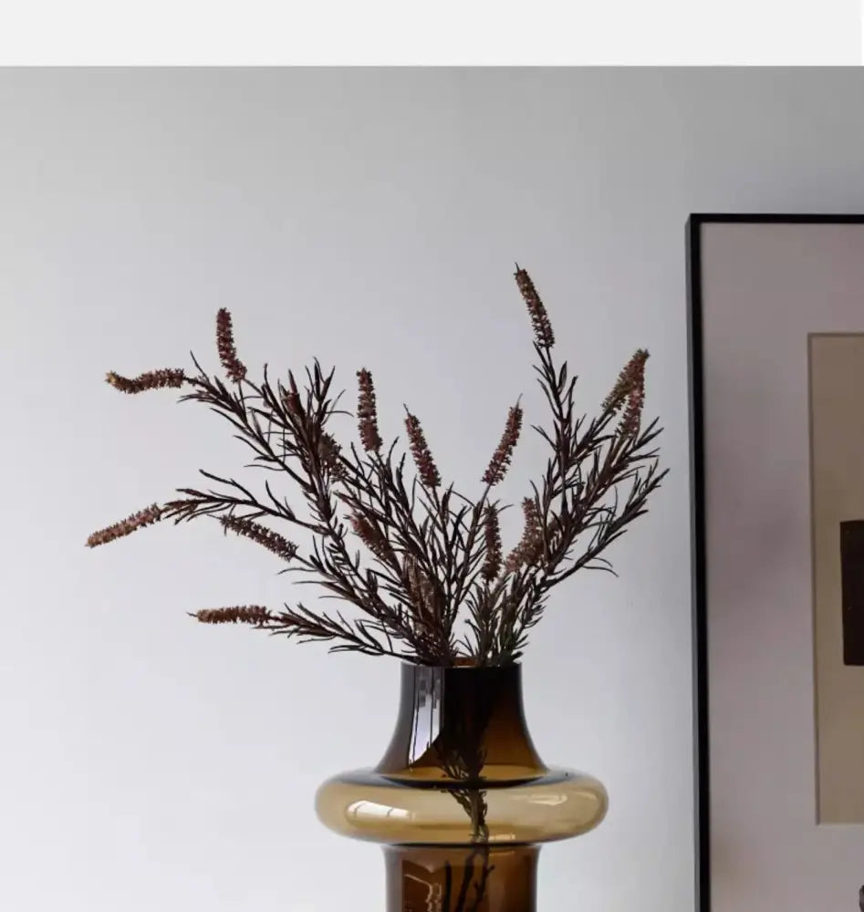 A sleek amber artisan glass vase with a flared neck and rounded base holding dried brown foliage