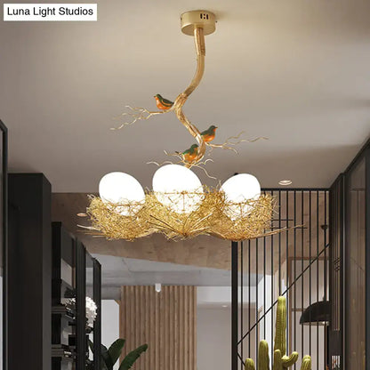 Golden bird-themed chandelier pendant with three milk white glass bulbs in a hand sewn aluminum nest design