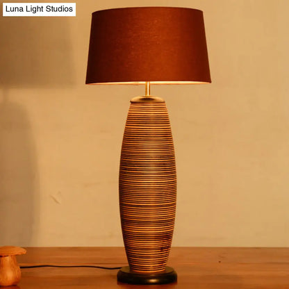 Lámpara de escritorio pequeña Asia Wood con luz de trabajo ovalada, color café y pantalla cilíndrica de tela.