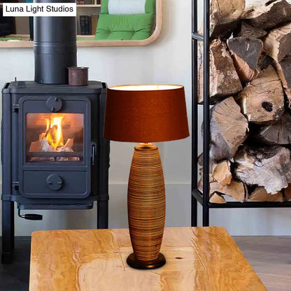 Lámpara de escritorio pequeña Asia Wood con luz de trabajo ovalada, color café y pantalla cilíndrica de tela.