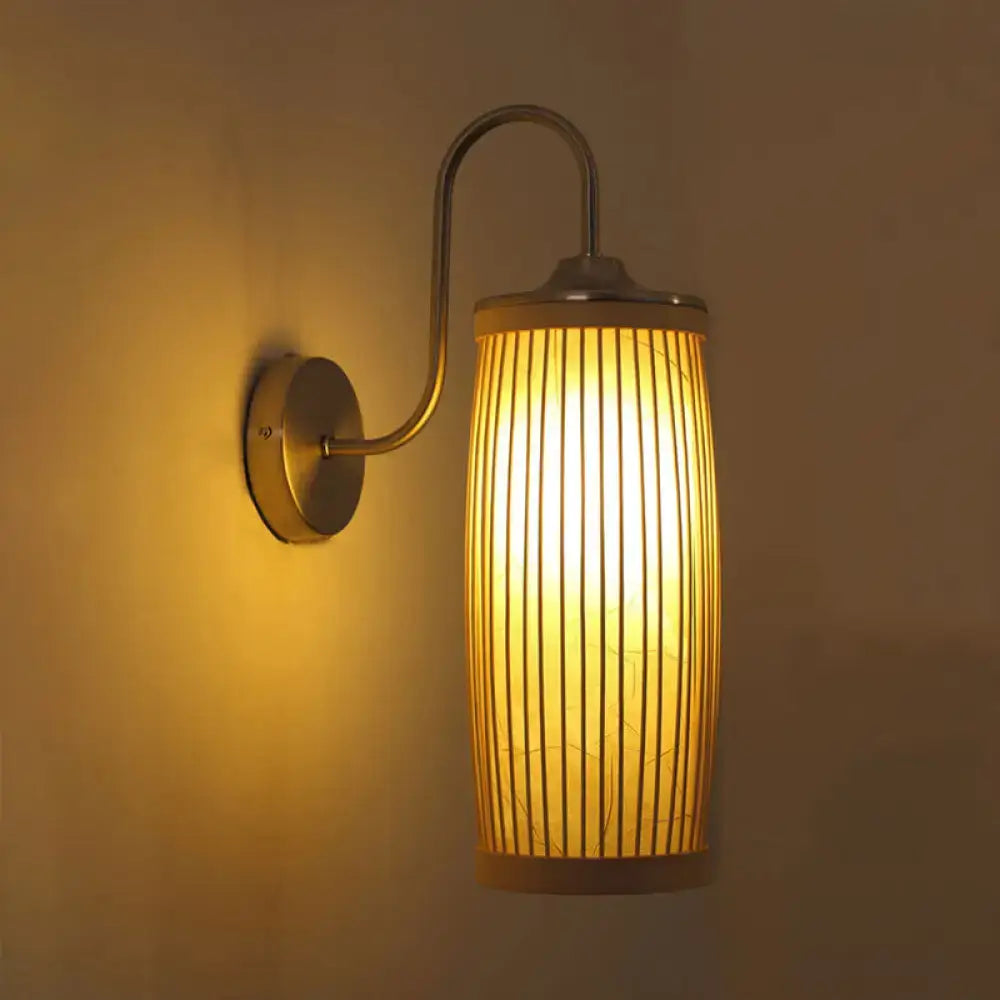 Warm-toned asian bamboo and brass wall lamp with cylindrical slats and curved gooseneck arm for bedroom sconce