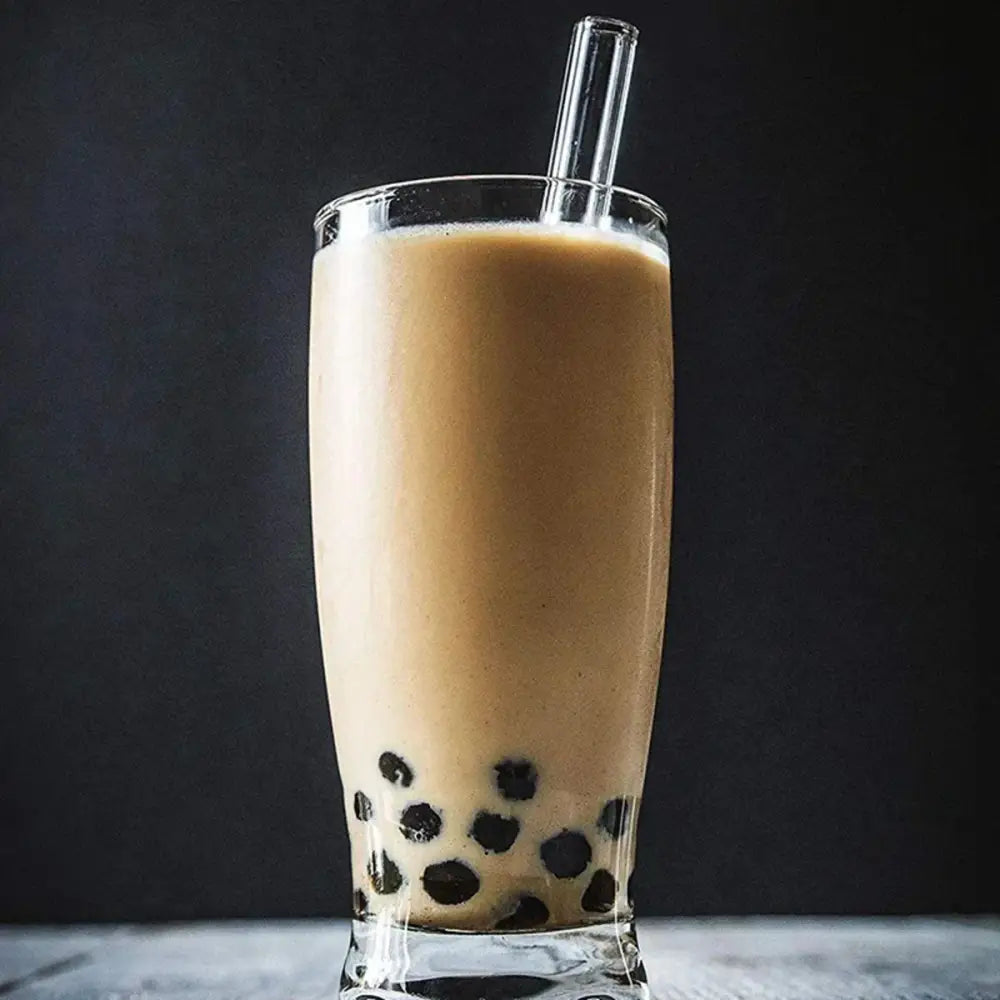 A tall clear glass filled with creamy brown bubble tea and black pearls alongside decorbites clear glass smoothie straws pack