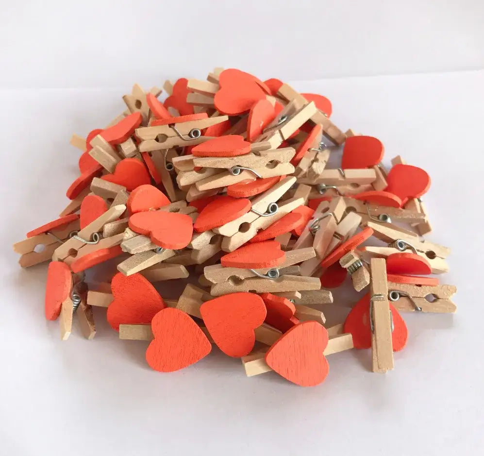 A pile of assorted mini wooden clips with bright orange heart shapes and natural wood bodies for bedroom photo decor