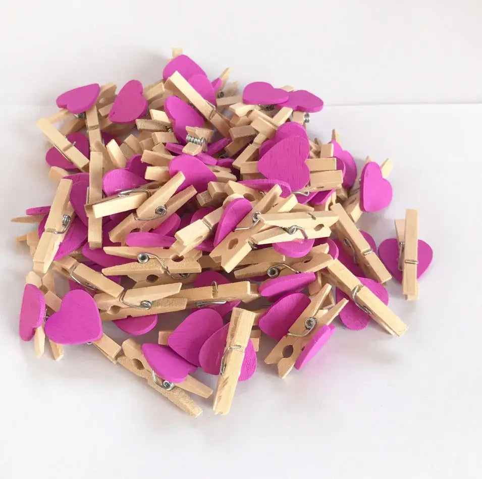 A pile of assorted colorful mini wooden clips with pink heart shapes and natural wood bodies for bedroom decor