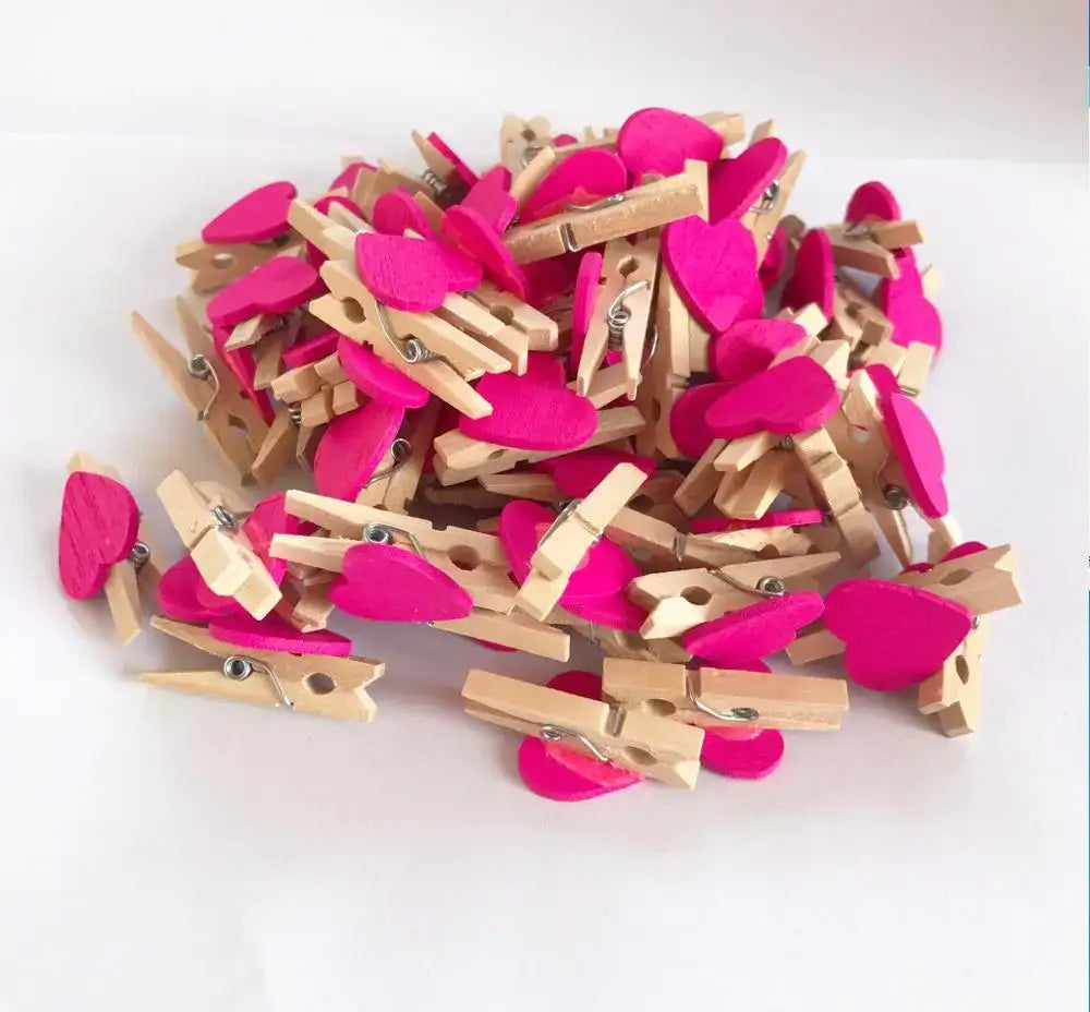 A pile of assorted colorful mini wooden clips with wooden heart shapes and vibrant pink felt accents for photo decor