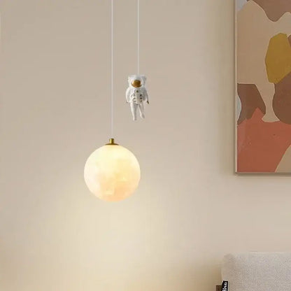 A whimsical white astronaut figurine hangs above a glowing white and gold led pendant light for bedrooms