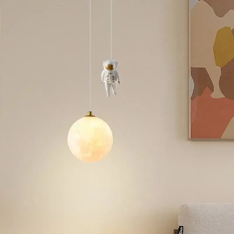 A whimsical white astronaut figurine hangs above a glowing white and gold led pendant light for bedrooms