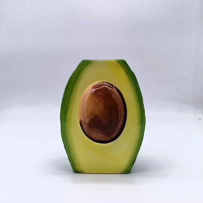 Glossy avocado ceramic vase shaped like a half-cut avocado with green skin, yellow flesh, and a detailed brown seed