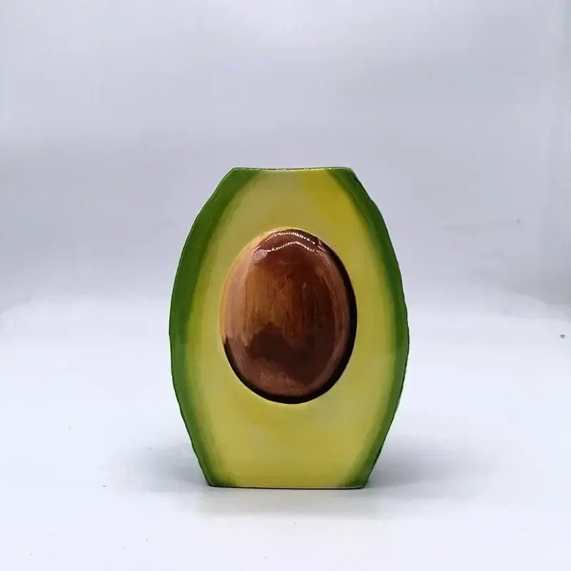 Glossy avocado ceramic vase shaped like a half-cut avocado with green skin, yellow flesh, and a detailed brown seed