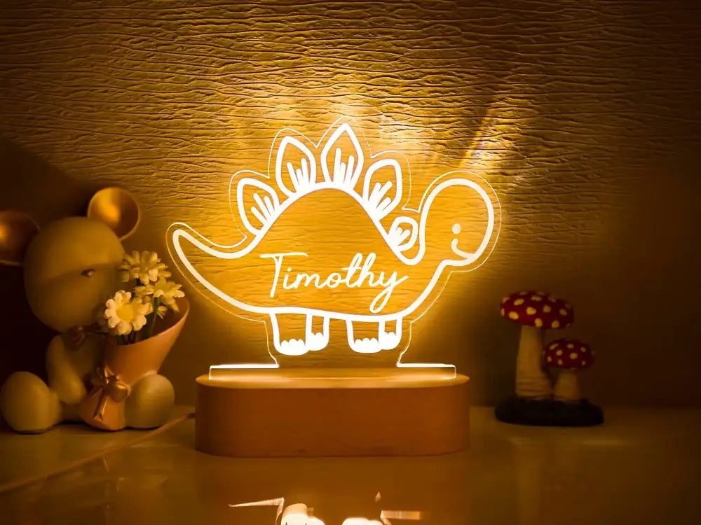 A glowing personalized dinosaur-shaped led night light with the name timothy in white cursive for baby kids decor