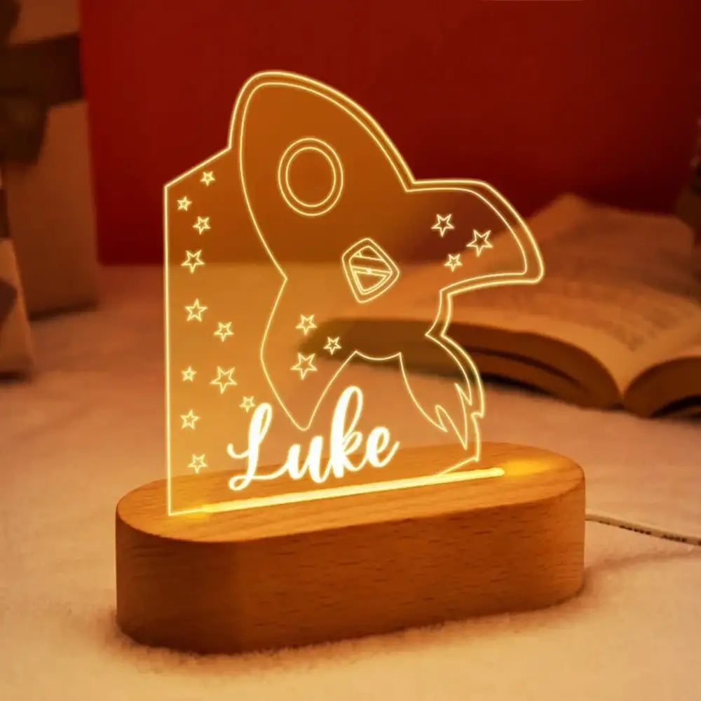A personalized rocket-shaped led night light with warm amber glow and luke etched on wooden base for baby kids bedroom