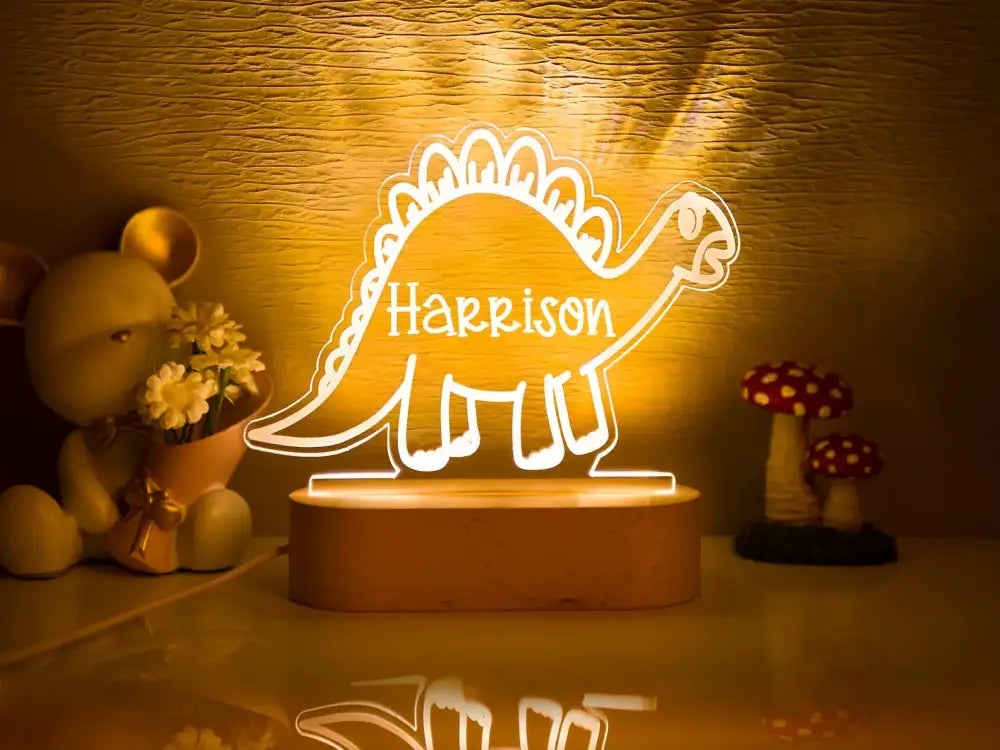 A glowing personalized stegosaurus-shaped led night light with the name harrison in white script for baby kids bedroom decor