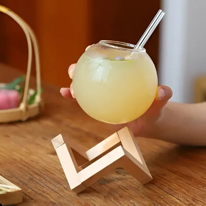 A clear glass ball shape coffee juice cocktail glass with transparent straw on a wooden stand for dining decor