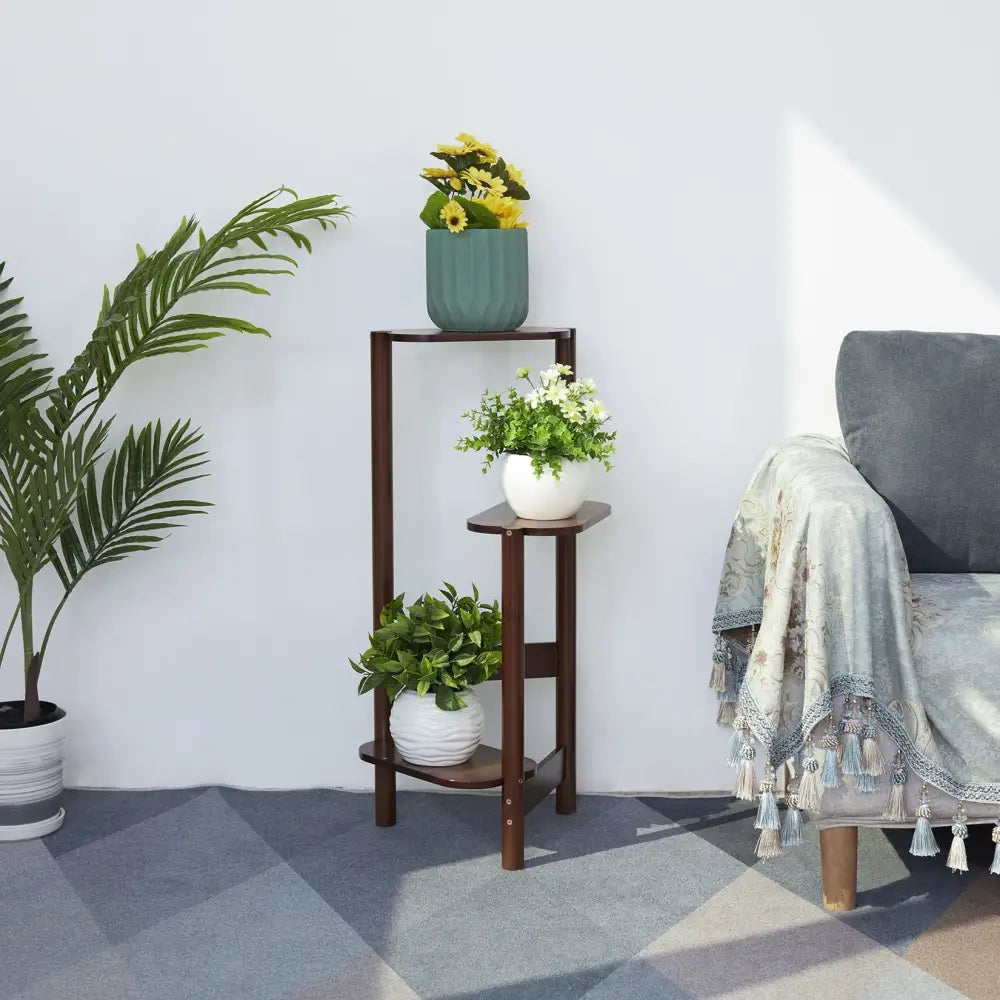Dark brown bamboo corner plant stand with three tiers rounded edges angled legs holding various potted plants