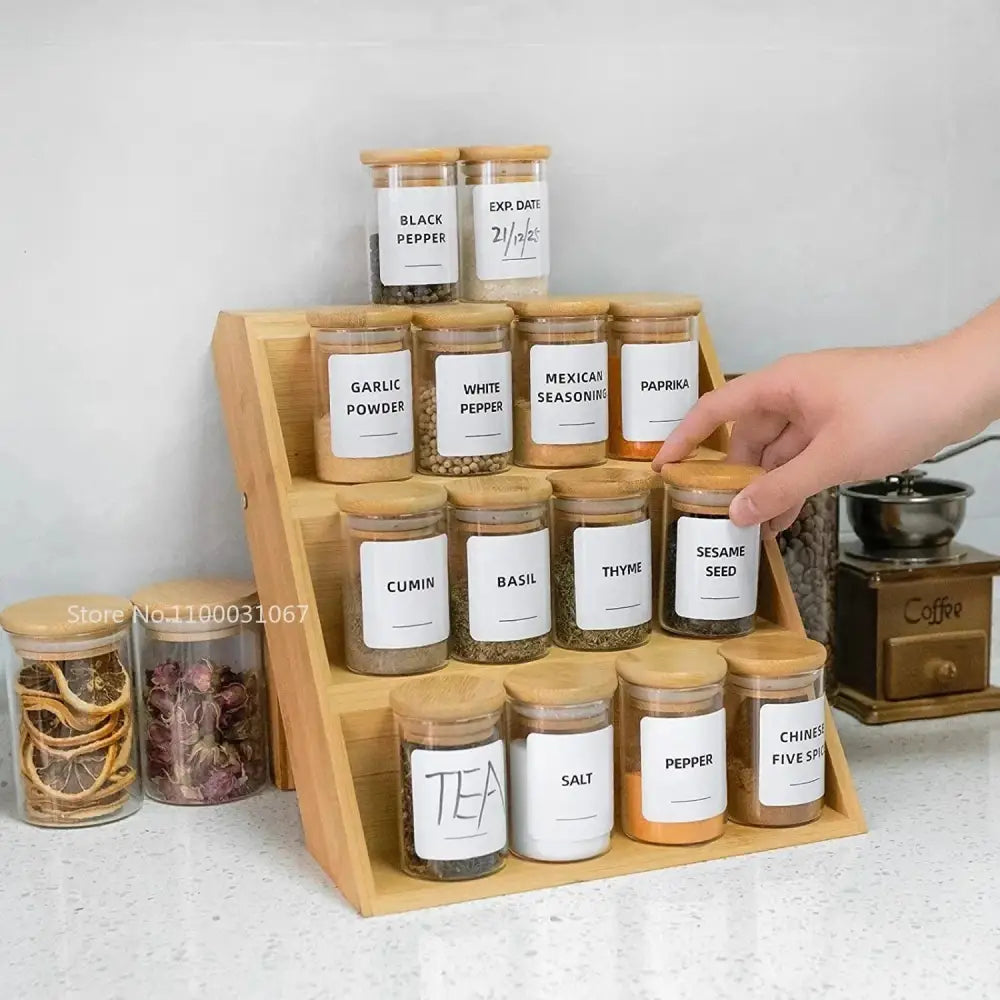 Wooden spice rack holding clear glass food storage jars with bamboo lids and white labels for kitchen use