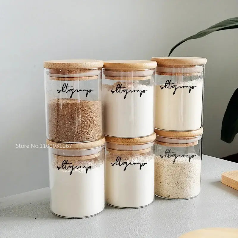 Clear glass food storage jars with bamboo lids and black cursive labeling for kitchen spice storage set