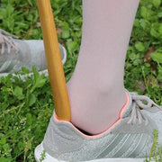 A light gray adidas sneaker with pink trim worn with pale pink socks shown with a bamboo pattern long handle shoe lifter