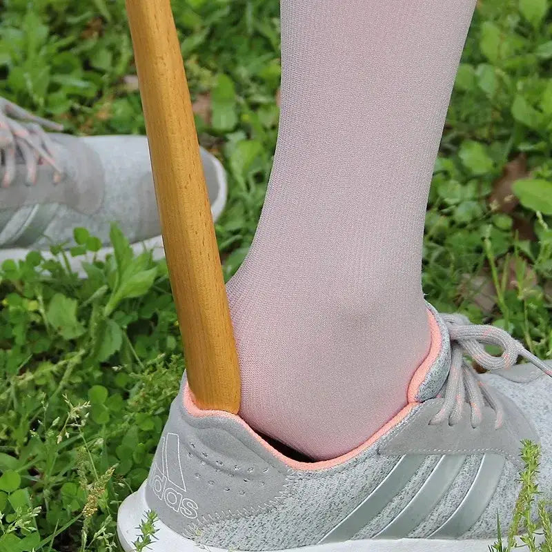 A light gray adidas sneaker with pink trim worn with pale pink socks shown with a bamboo pattern long handle shoe lifter
