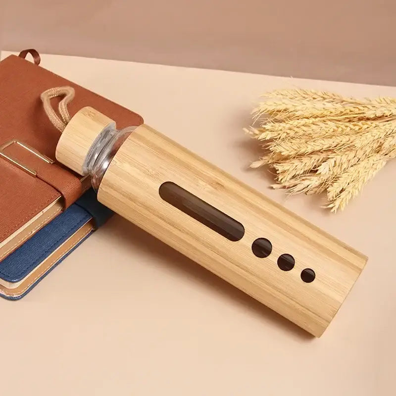 A sleek bamboo-finished glass water bottle with natural wood grain, wooden cap, and circular cutouts for sports use
