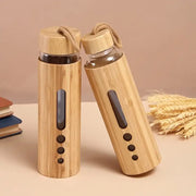 Two bamboo-wrapped glass water bottles with wooden lids and rope handles featuring transparent windows and cutouts