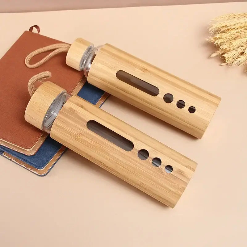 Two bamboo-finished glass water bottles with wooden caps and handles featuring cutouts for kitchen and sports use