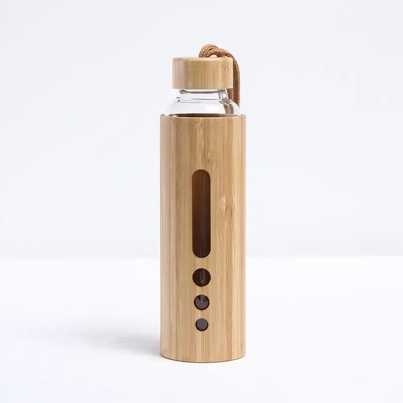 A clear glass water bottle in a light bamboo sleeve with cutouts and a matching bamboo lid with woven strap for sports use
