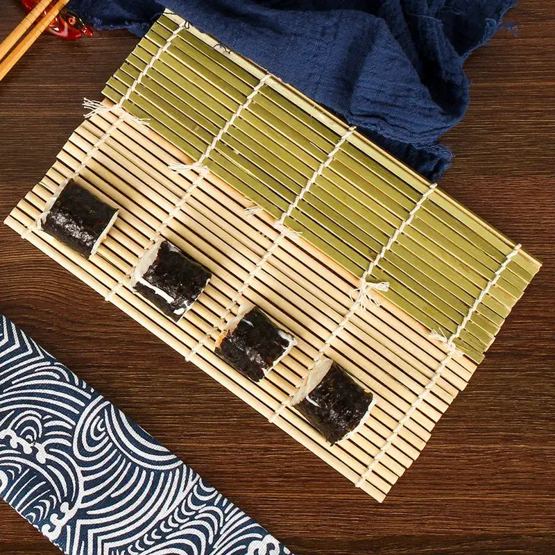 A bamboo sushi rolling mat with greenish hue natural wood grain and white twine for sushi rolling and onigiri rice paddles