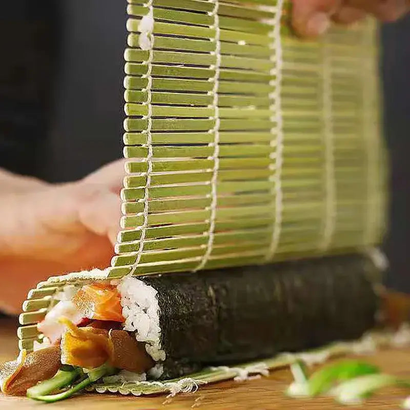 Green bamboo sushi rolling mat used for sushi rolling with rice nori and fillings alongside onigiri rice paddles kitchen tool