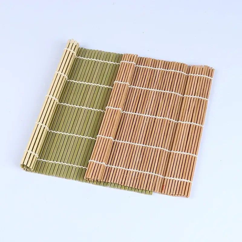 Two bamboo sushi rolling mats in natural tan and olive green with white string bindings for sushi rolling and onigiri rice paddles