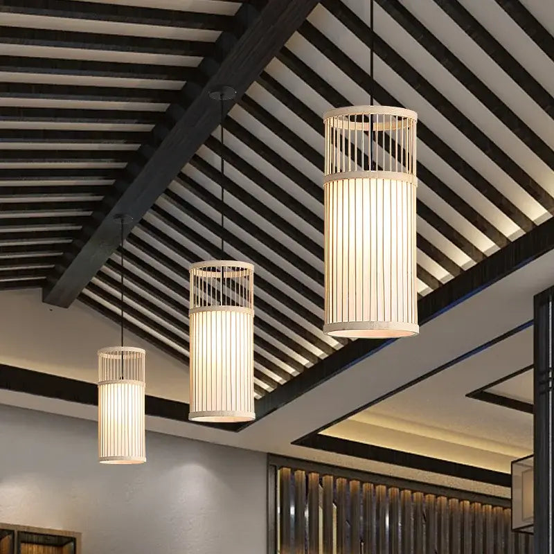 Three cylindrical bamboo wooden pendant lamps with vertical slats and warm glowing illumination for kitchen bar use