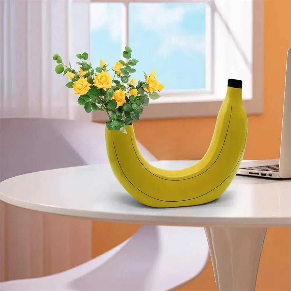 A bright yellow banana shape resin flower vase with a black cap holding yellow roses and green foliage