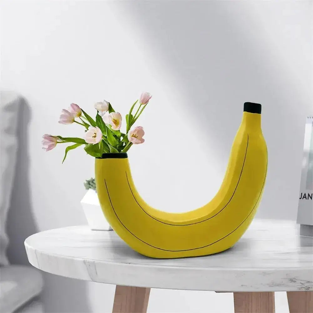 A bright yellow banana shape resin flower vase with black stem holding pink tulips for decorative use
