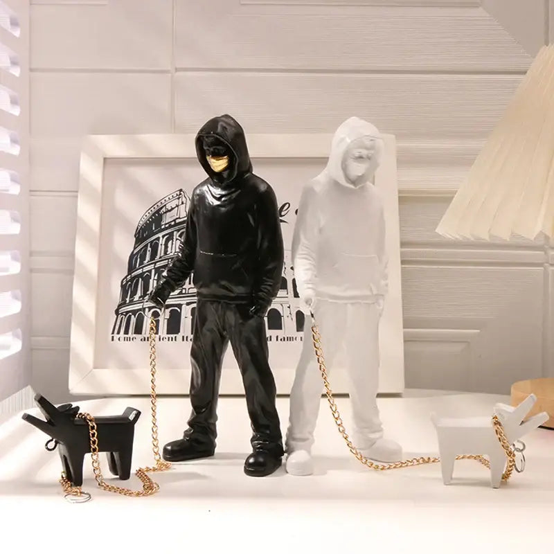 Black and white banksy dog walker resin statue featuring hooded figures with gold-trimmed chains and dog keychains