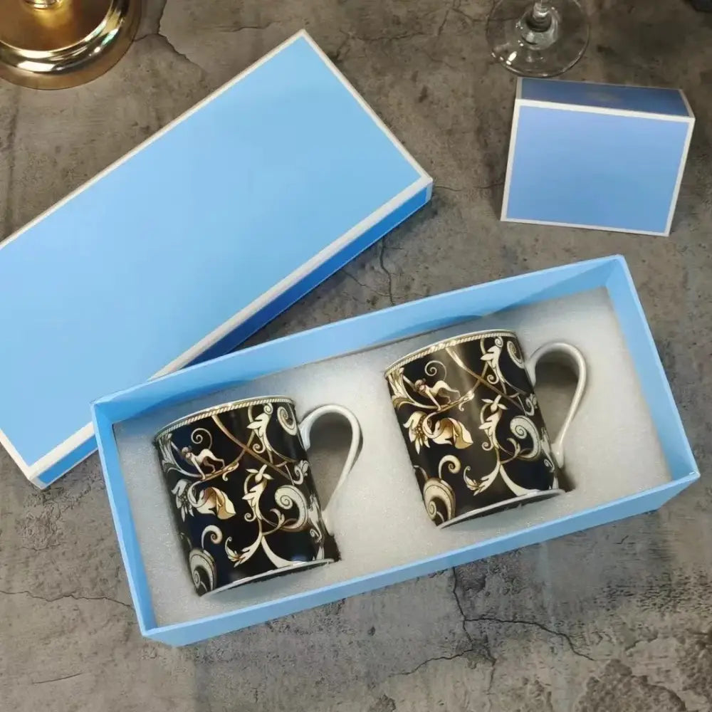 Pair of black ceramic mugs with gold and white ornate floral patterns in a light blue box from the black unicorn series