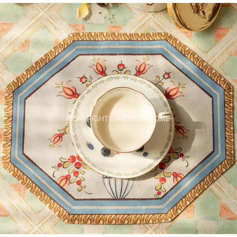 White ceramic teacup with gold rim and floral pattern on matching saucer with decorbites baroque flowers fringe placemat set
