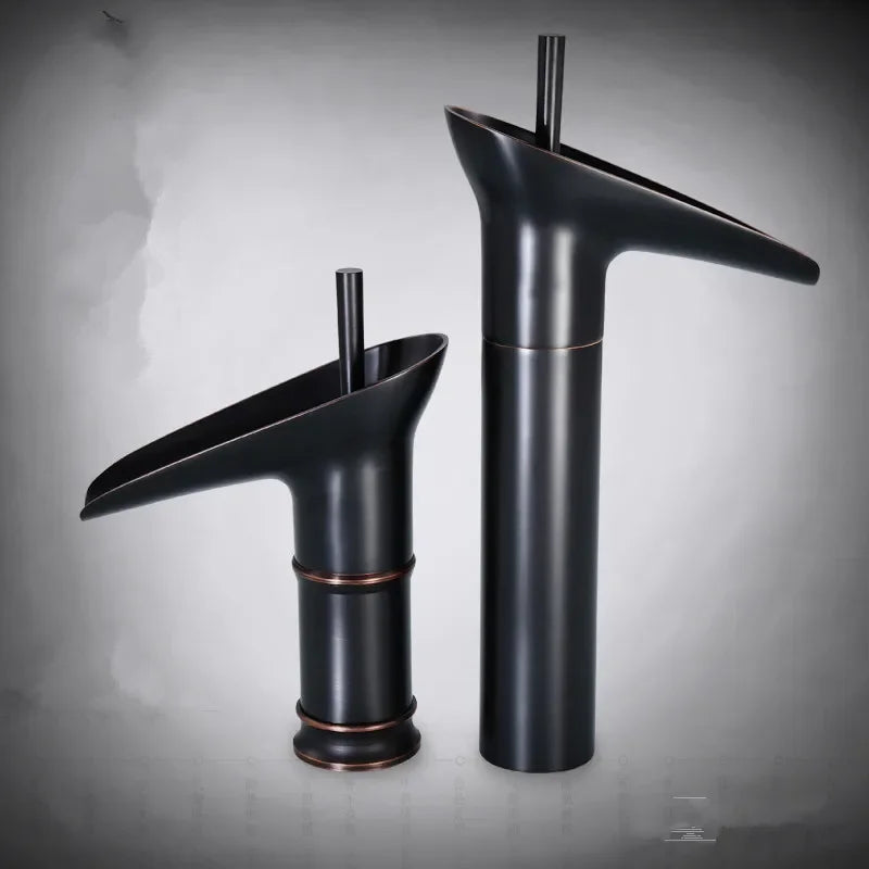 Two matte black deck mounted bathroom faucets with copper accents featuring antique brass waterfall spouts and metered valve control