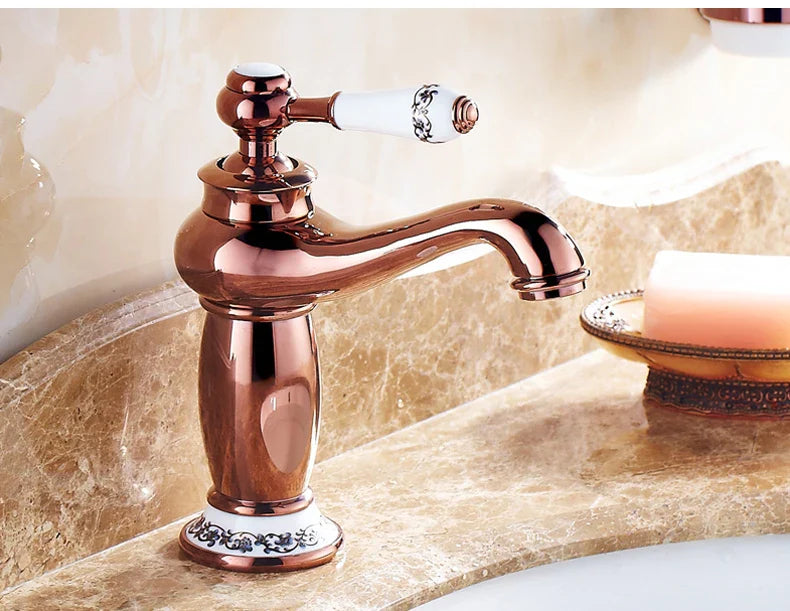 Antique brass-finished bathroom faucet with white ceramic handle and ornate black floral detailing in bronze finish