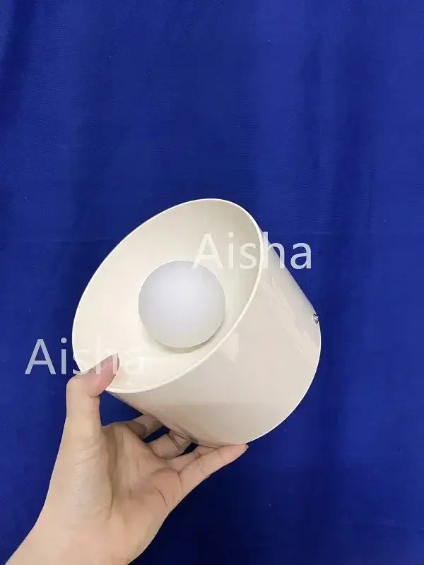 Cream-colored ceramic bowl with glossy finish holding matching sphere beside bauhaus black and white metal wall lamp sconce