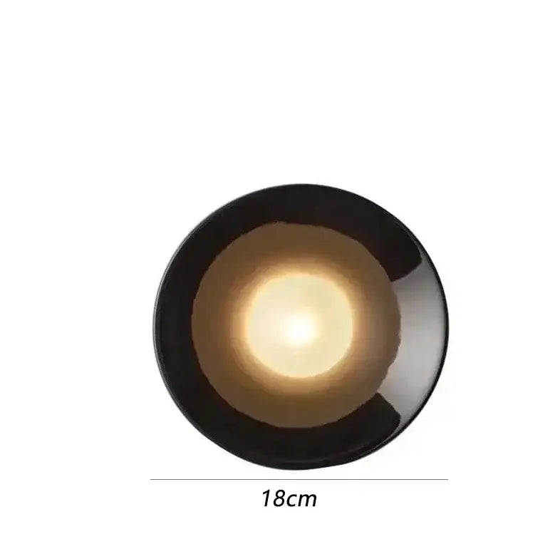 A sleek bauhaus metal wall lamp in black with a glossy finish and illuminated central glow for living room use