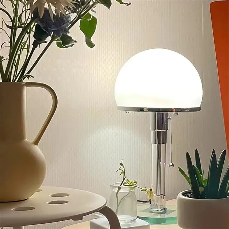 A bauhaus chrome table lamp with a sleek finish and a smooth milk white glass spherical shade for bedroom use
