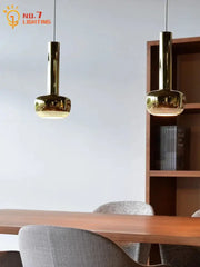 Two sleek gold bauhaus copper chrome pendant lights with cylindrical stems hang above a wooden kitchen island table