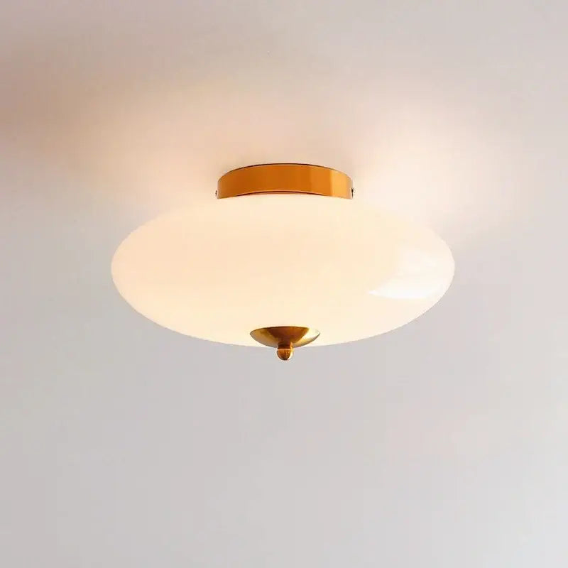 A sleek modern ceiling lamp with cream white glass shade and warm brass finish ideal for dining room decorbites