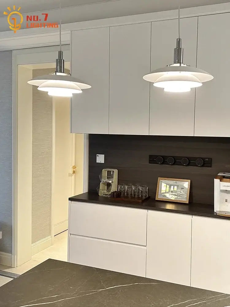 Two sleek white bauhaus flying saucer pendant lights with polished chrome fixtures hang above a kitchen island
