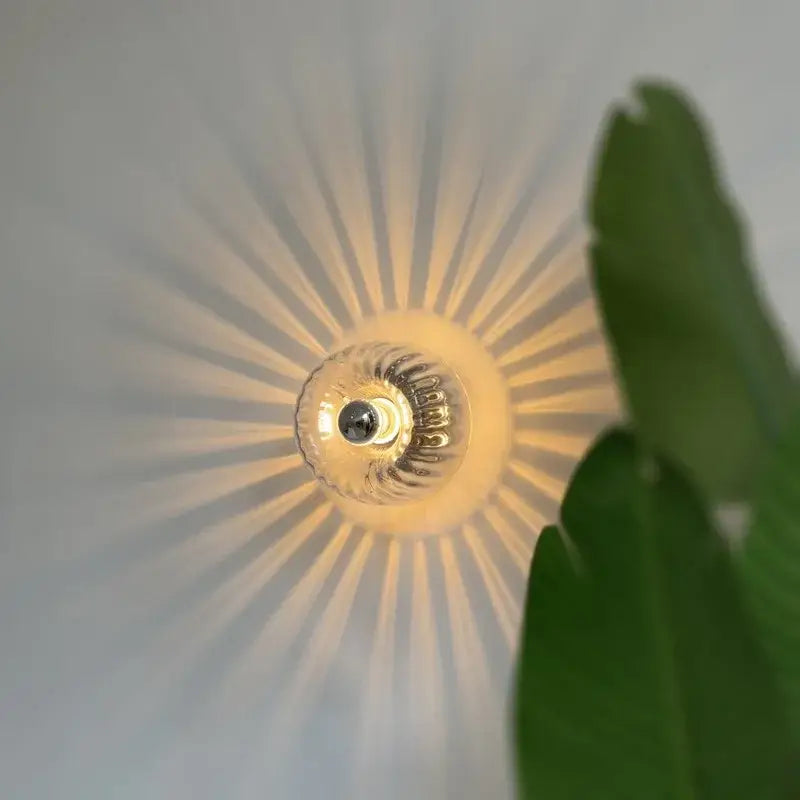 A warm glowing bauhaus glass e14 wall lamp with ribbed clear glass shade and metallic base for living room use
