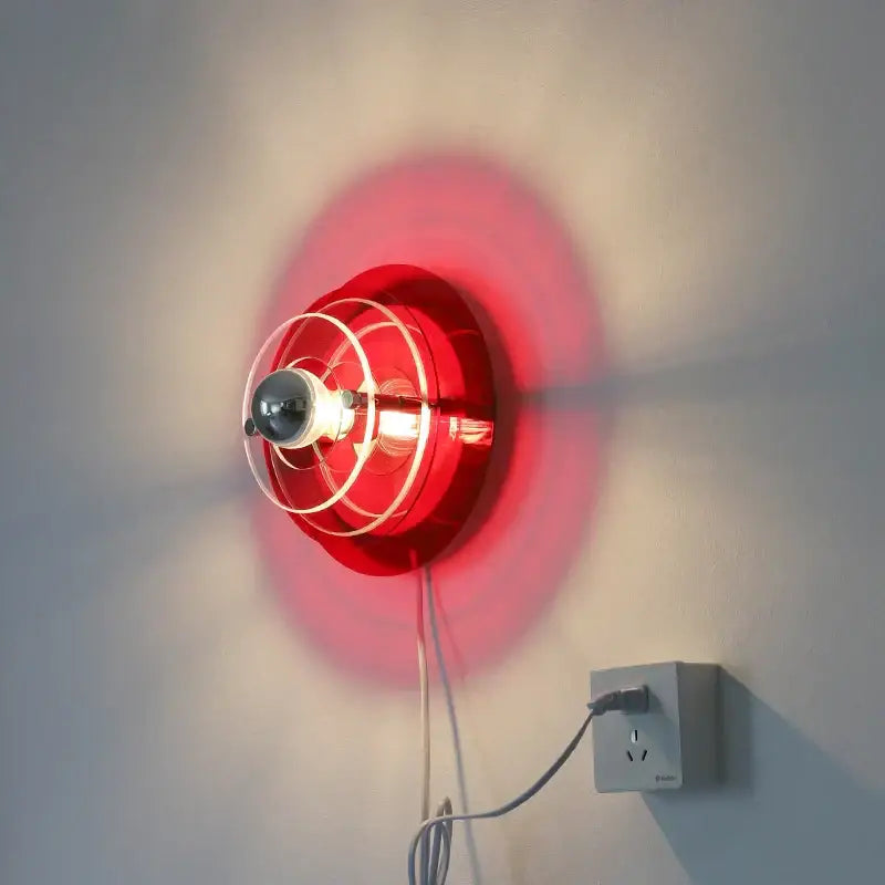 Vibrant red circular bauhaus led wall sconce with clear glass cage and exposed bulb for bedroom or living room use
