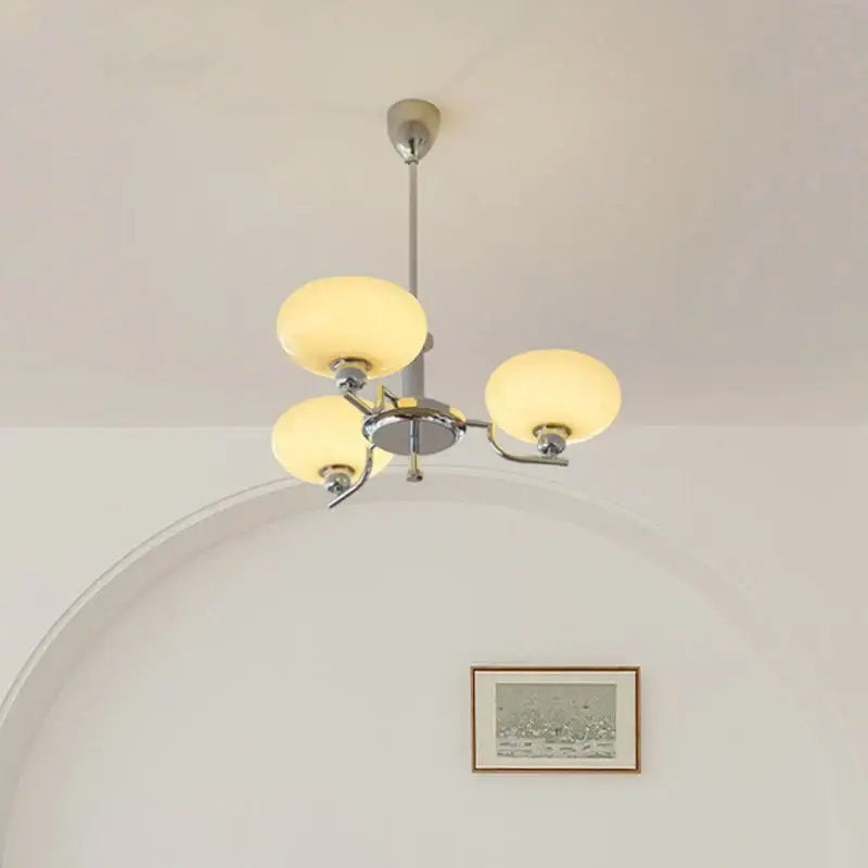 A bauhaus medieval chandelier with a chrome finish and three warm frosted glass shades for living room lighting