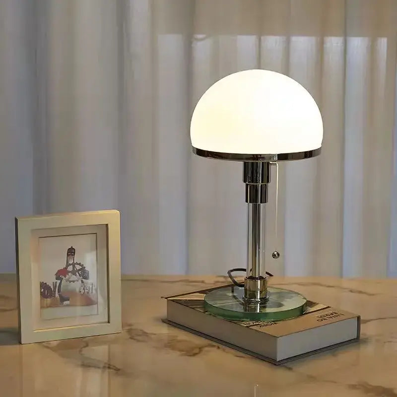 A bauhaus mushroom table lamp with a chrome finish, milk white glass dome shade, and circular glass base for bedroom lighting